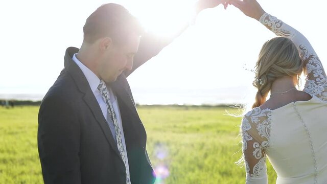 Groom Hold The Bride's Hand As She Spins Around Herself  In Her Elegant White Dress On Bright Sunshine Meadow - Medium Shot (Slow Motion)
