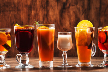 Selection of autumn or winter alcoholic hot drinks and cocktails - mulled wine, glogg, grog, eggnog, warm ginger ale, hot buttered rum, punch, mulled apple cider on wood background, copy space
