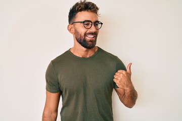 Young hispanic man wearing casual clothes and glasses smiling with happy face looking and pointing...