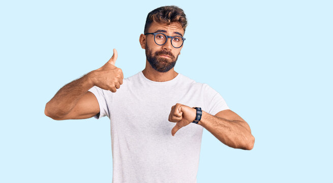 Young hispanic man wearing casual clothes and glasses doing thumbs up and down, disagreement and agreement expression. crazy conflict