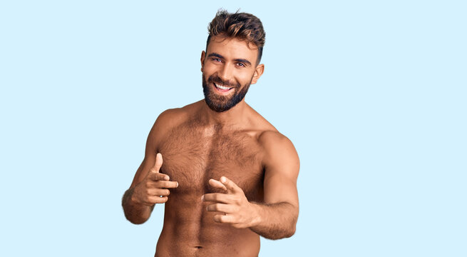 Young hispanic man wearing swimwear shirtless pointing fingers to camera with happy and funny face. good energy and vibes.