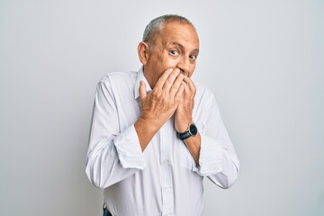 Handsome senior man wearing casual white shirt laughing and embarrassed giggle covering mouth with...
