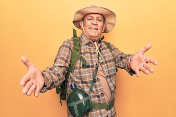 Fototapeta premium Senior man with grey hair wearing hiker backpack and water canteen looking at the camera smiling with open arms for hug. cheerful expression embracing happiness.