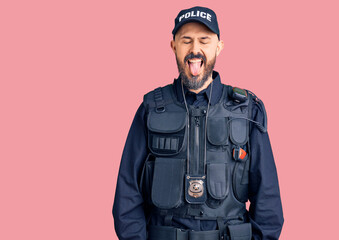Young handsome man wearing police uniform sticking tongue out happy with funny expression. emotion concept.