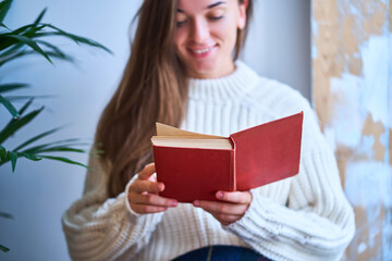 Cozy woman in knitted white warm sweater reading a book