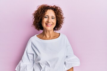 Beautiful middle age mature woman wearing elegant clothes over pink background looking positive and...