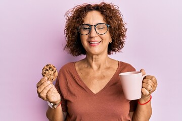 Beautiful middle age mature woman drinking a cup of coffee and cookie winking looking at the camera...