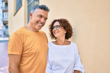 Middle age couple smiling happy leaning on the wall at street of city.