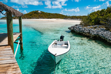 Small boat moored off a pier over turquoise ocean waters near private remote Exuma Islands in the Bahamas - Powered by Adobe