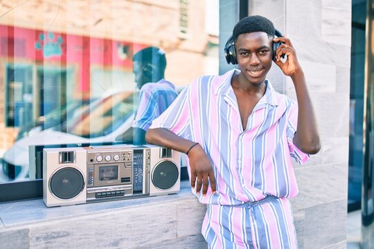 Young african american man listening to music using boom box and headphones leaning on the wall.