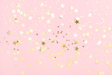 Pink pastel festive background with shining golden confetti in shape of stars.
