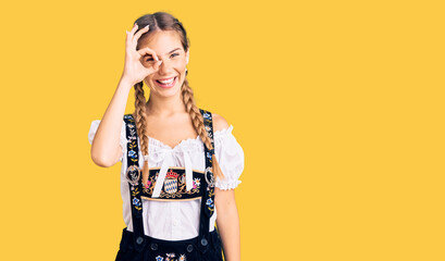 Beautiful caucasian woman with blonde hair wearing octoberfest traditional clothes doing ok gesture with hand smiling, eye looking through fingers with happy face.