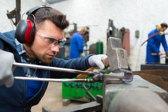 Worker In Factory With Hammer On Work Bench