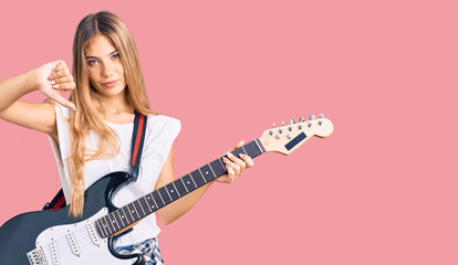 Fototapeta premium Beautiful caucasian woman with blonde hair playing electric guitar with angry face, negative sign showing dislike with thumbs down, rejection concept