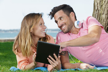 the couple lay on the grass and hold an laptop