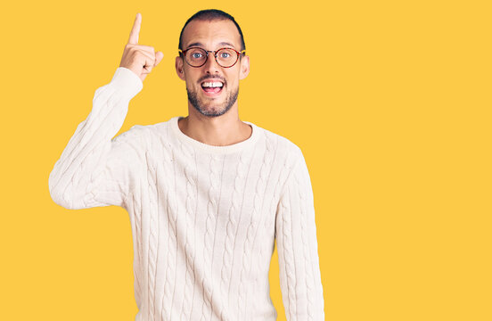 Young handsome man wearing casual clothes and glasses pointing finger up with successful idea. exited and happy. number one.