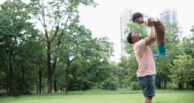 African father spends time and have fun together with his son. Young dad with beard and mustache carried his little boy in the air at garden green park on weekend