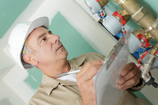 matue plumber with clipboard stood by pipework