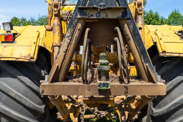 Closeup of a yellow tractor with heavy wheels in a field with trees in background