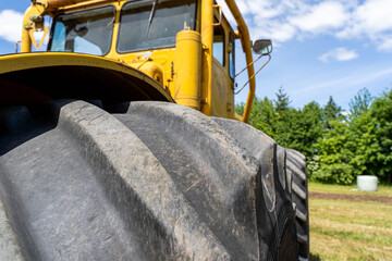 Closeup of a yellow tractor with heavy wheels in a field with trees in background