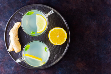 Ginger tea with lemon on a dark background. Two cups of ginger tea on a black plate. Copy space. Top view