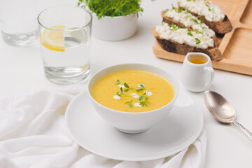 squash soup, soft cheese sandwich on a board and glass of water on background
