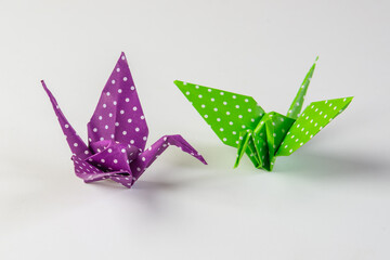 Two origami crain birds made from green and purple paper with white dots, isolated on blank background