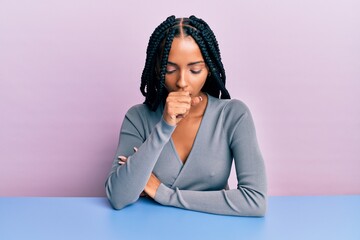 Beautiful hispanic woman wearing casual clothes sitting on the table feeling unwell and coughing as...