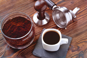 coffee in a cup on a stone stand, glass jar with coffee and coffee accessories tempera and a horn for a coffee machine, wooden natural background, tinted