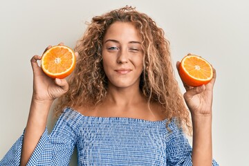 Beautiful caucasian teenager girl holding fresh orange winking looking at the camera with sexy...
