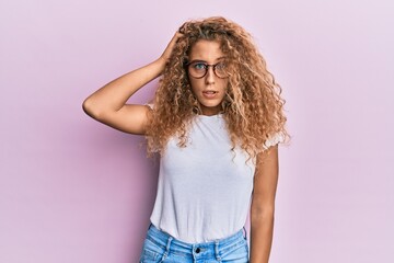 Beautiful caucasian teenager girl wearing white t-shirt over pink background confuse and wonder about question. uncertain with doubt, thinking with hand on head. pensive concept.