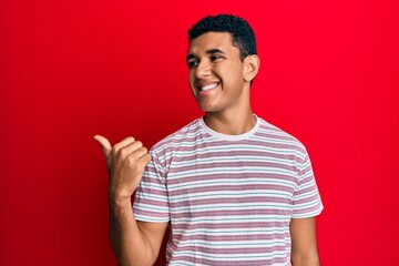 Young arab man wearing casual clothes pointing thumb up to the side smiling happy with open mouth