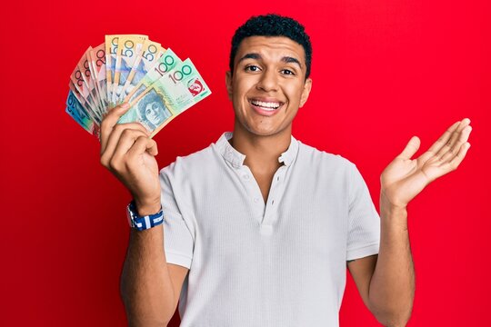 Young arab man holding australian dollars celebrating achievement with happy smile and winner expression with raised hand