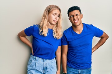 Young interracial couple wearing casual clothes suffering of backache, touching back with hand, muscular pain