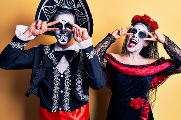 Young couple wearing mexican day of the dead costume over yellow doing peace symbol with fingers...