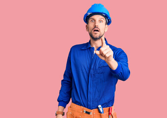 Young handsome man wearing worker uniform and hardhat pointing displeased and frustrated to the camera, angry and furious with you