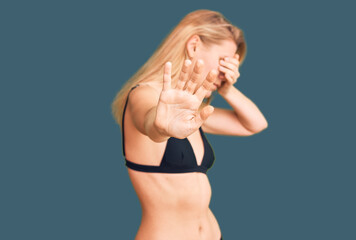 Young beautiful blonde woman wearing bikini covering eyes with hands and doing stop gesture with sad and fear expression. embarrassed and negative concept.