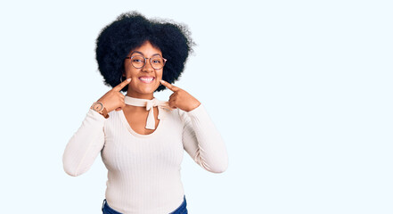 Young african american girl wearing casual clothes and glasses smiling with open mouth, fingers pointing and forcing cheerful smile