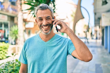 Middle age grey-haired man talking on the smartphone walking at street of city.