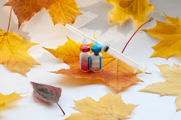 Yellow maple leaves on the sheet in the middle there is a syringe and two vials with the vaccine....