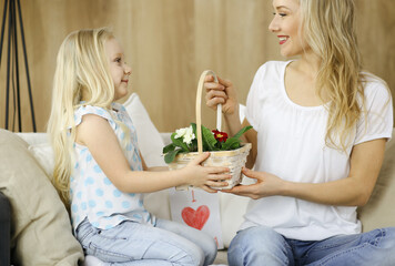 Happy mother day Child daughter congratulates mom and gives her basket of spring flowers and postcard with heart drawing. Family and childhood concepts