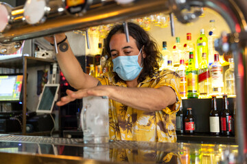 Portrait of a caucasian waiter working in a bar. He is wearing a medical mask. New normal concept.