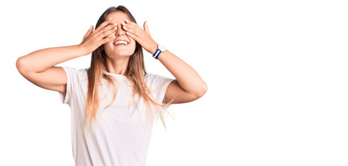 Beautiful caucasian woman wearing casual white tshirt covering eyes with hands smiling cheerful and funny. blind concept.