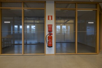 View of two empty office rooms with glass walls. Red fire extinguisher on white wall between offices.