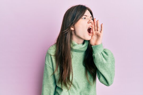 Young beautiful caucasian girl wearing wool sweater shouting and screaming loud to side with hand on mouth. communication concept.