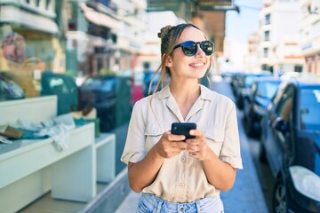 Young beautiful blonde caucasian woman smiling happy outdoors on a sunny day using smartphone