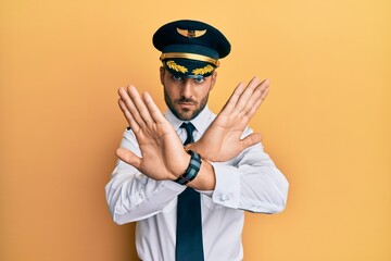 Handsome hispanic man wearing airplane pilot uniform rejection expression crossing arms doing negative sign, angry face © Krakenimages.com
