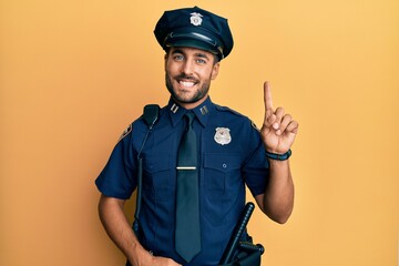 Handsome hispanic man wearing police uniform showing and pointing up with finger number one while smiling confident and happy.