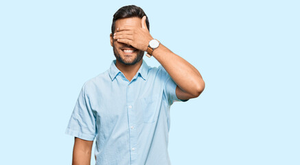 Fototapeta premium Handsome hispanic man wearing casual clothes smiling and laughing with hand on face covering eyes for surprise. blind concept.