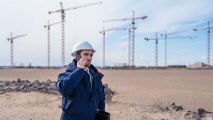 a civil engineer in a white helmet is talking on the phone in the background of construction.